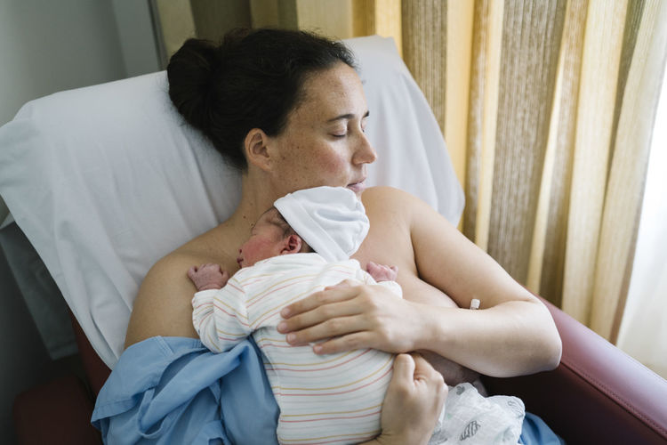 Mother embracing newborn baby boy while resting