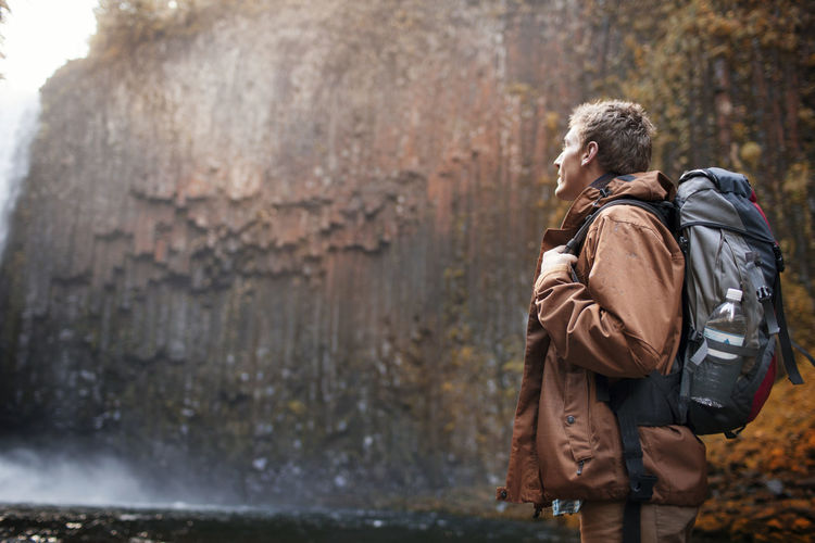Male hiker carrying backpack while looking at waterfall