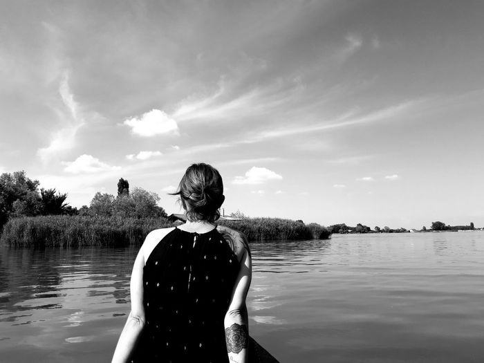 Rear view of woman standing in lake against sky