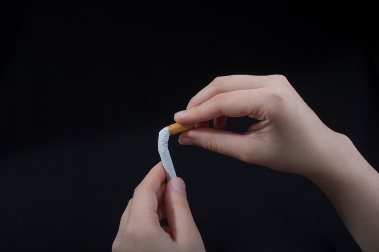 Close-up of hand crushing cigarette over black background