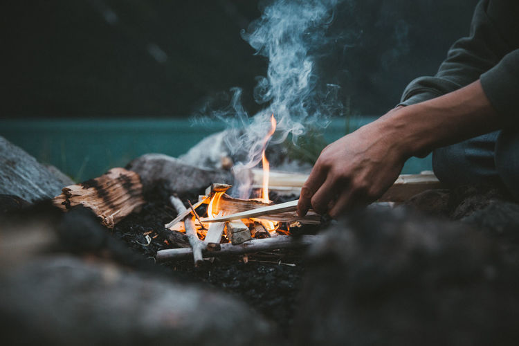 Midsection of man sitting by campfire