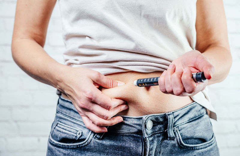 A woman injects insulin with insulin injection device into the subcutaneous tissue of abdomen