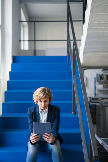 Female entrepreneur using digital tablet while sitting on steps in factory