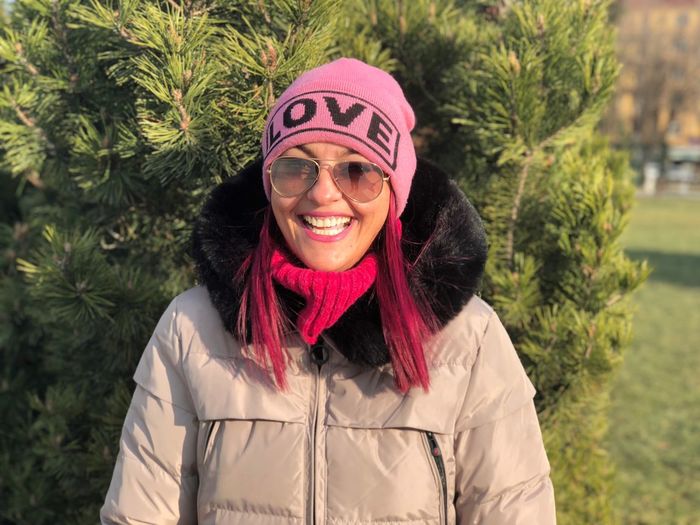 Portrait of smiling woman in sunglasses and knit hat against tree