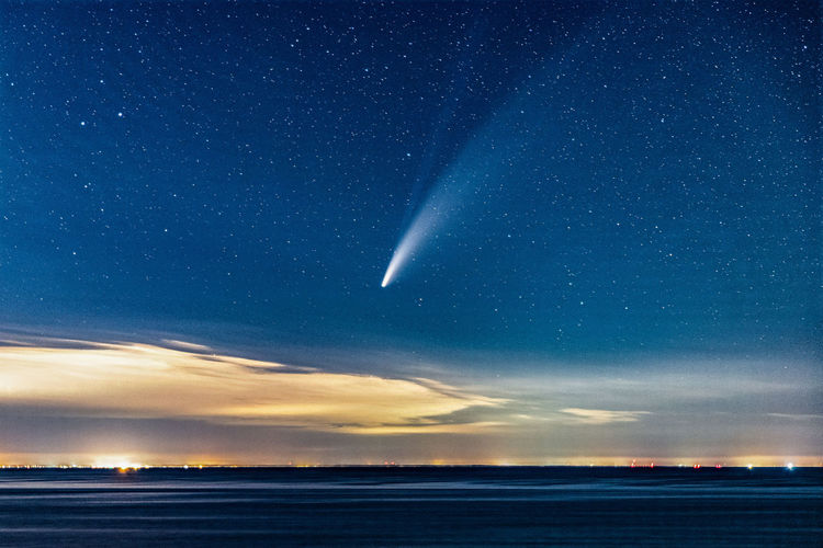 Comet neowise streaking through the sky above the ocean after sunset.