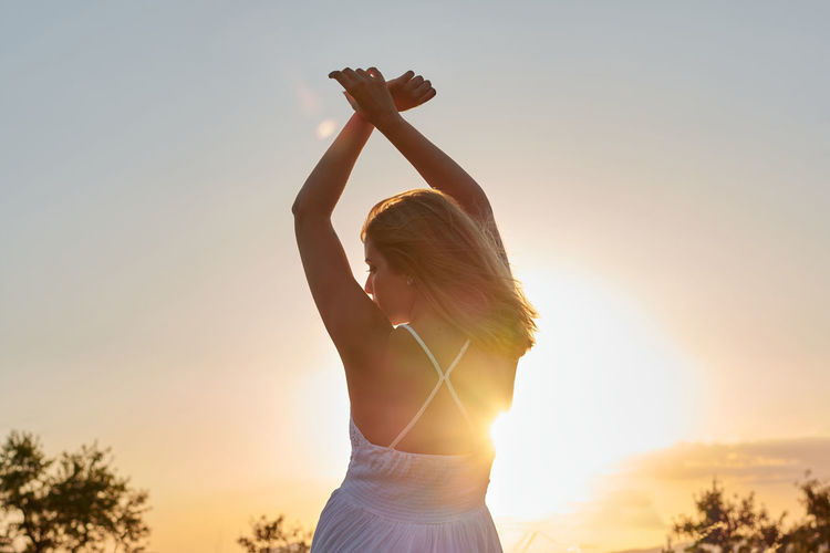 Woman with arms raised standing against sky during sunset