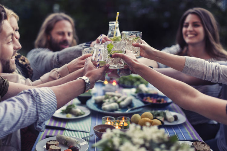 Happy friends toasting mojito glasses at dinner table in yard