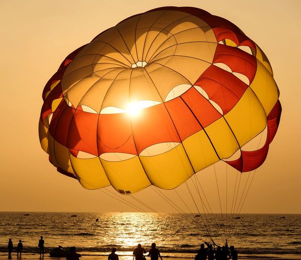 Silhouette people standing below parachute against sea at beach