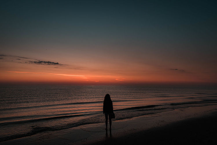Silhouette woman standing on beach against sky during sunset