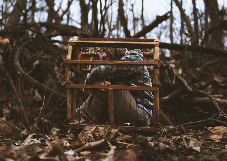 Side view of woman locked in cage at forest