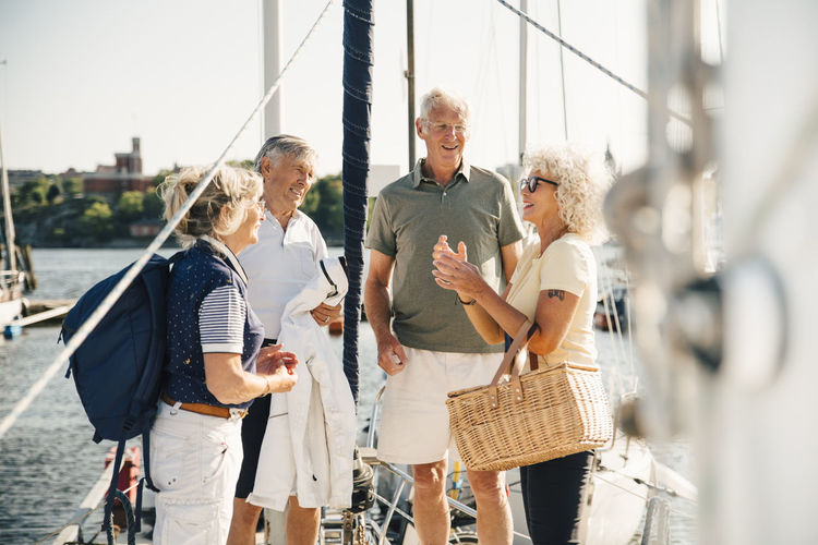 Male and female senior friends talking with each other while standing in boat on sunny day