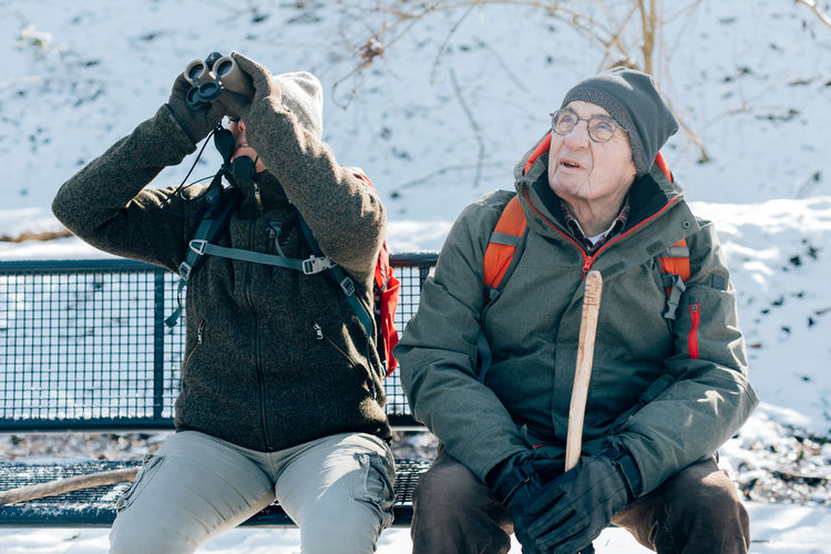 Senior people sitting on bench outdoor in winter - elderly couple hiking in the snow