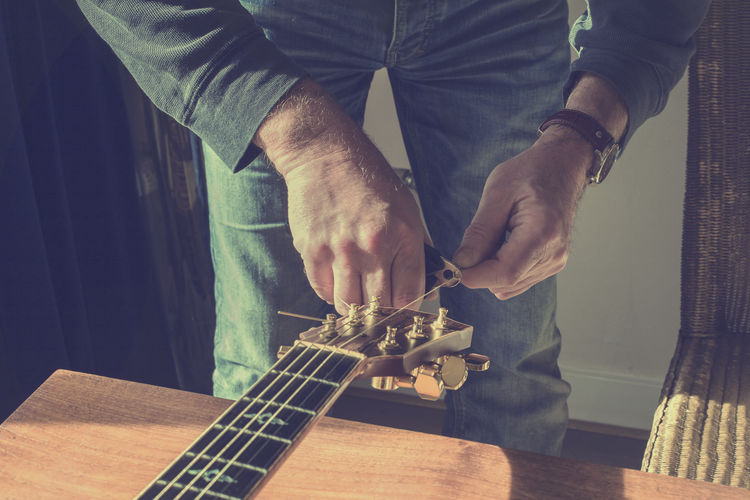 Midsection of man repairing guitar by table