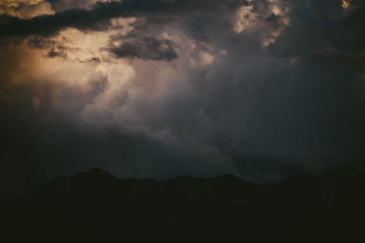 Low angle view of storm clouds over silhouette mountain