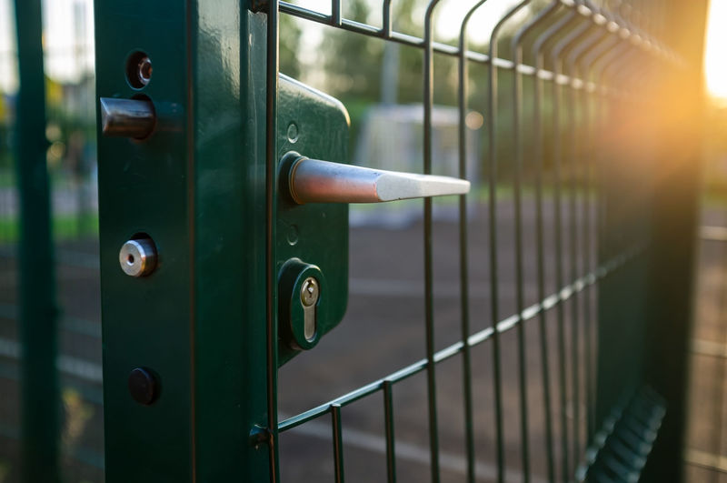 Handle with lock on open gate of sports ground fenced with a welded mesh fence outdoors at sunset