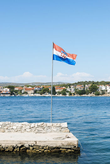 Flag by sea against clear blue sky