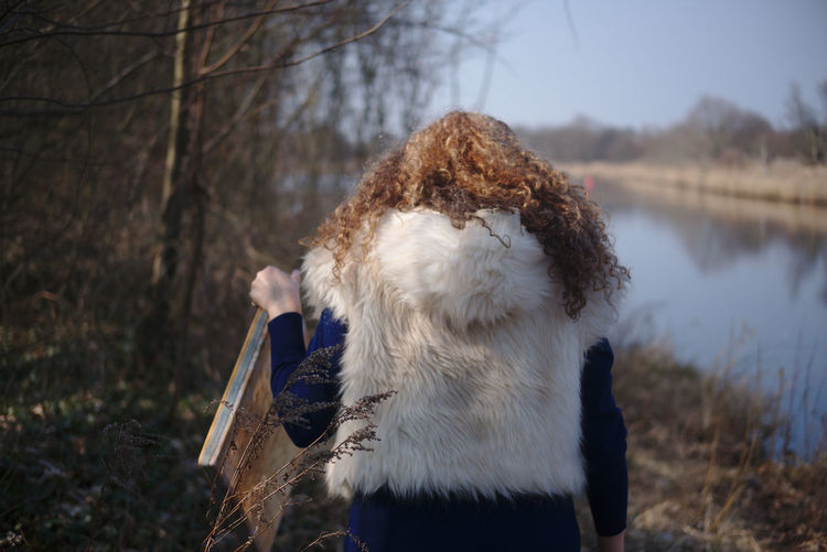 Rear view of woman in fur coat standing at lakeshore