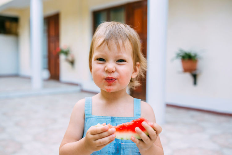 Little cute cheerful girl eating a slice of watermelon close up.