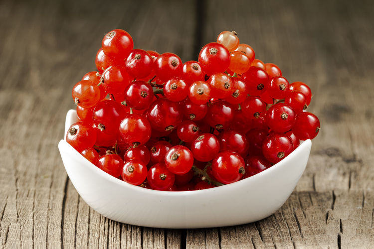 Fresh red currants in a white ceramic bowl on a dark brown wooden table