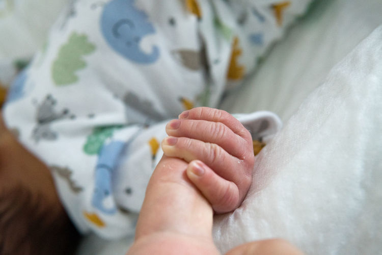 Cropped image of baby hand on bed