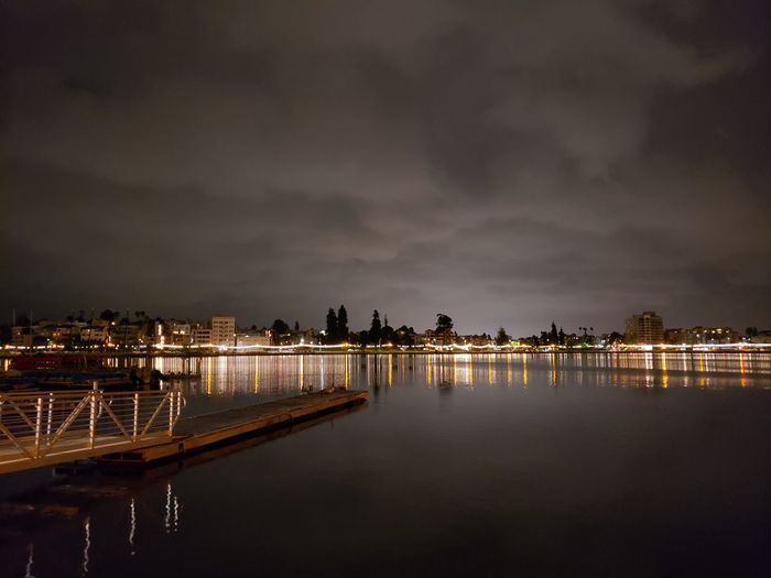 Illuminated buildings by river against sky at night