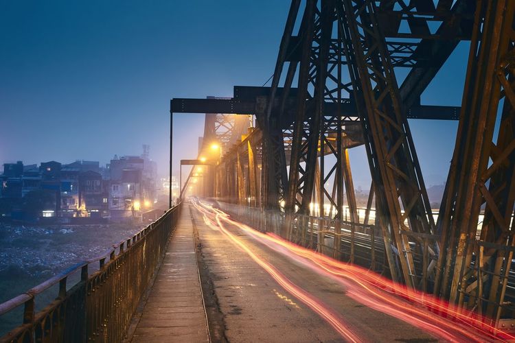 Light trails on bridge in city at dusk