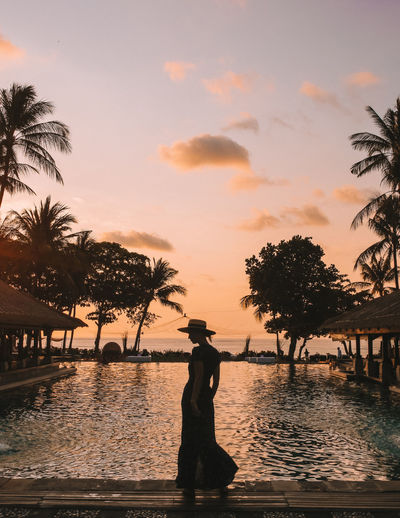 Silhouette woman walking against swimming pool during sunset