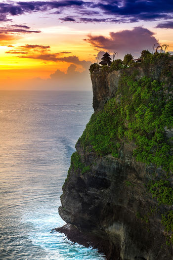 Uluwatu temple on cliff by sea against sky during sunset