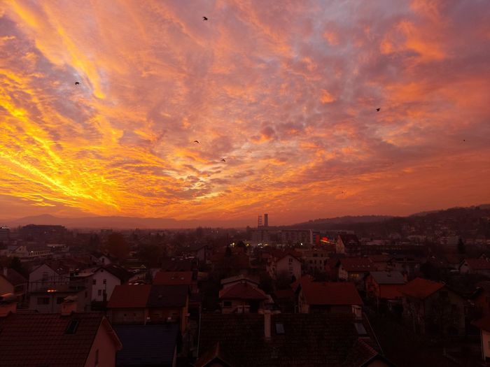 High angle view of townscape against orange sky and view of flying birds