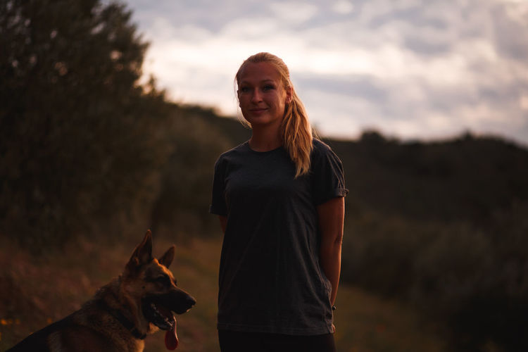 Portrait of woman with dog standing against sky during sunset
