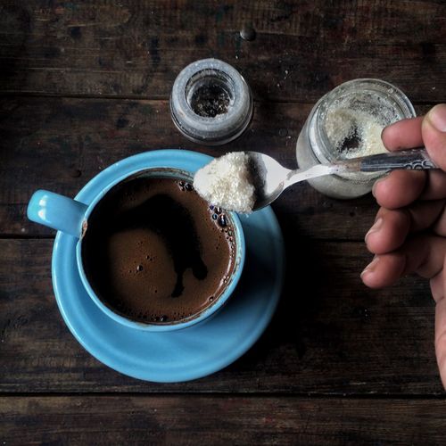 Cropped hand of person adding sugar in black coffee at table