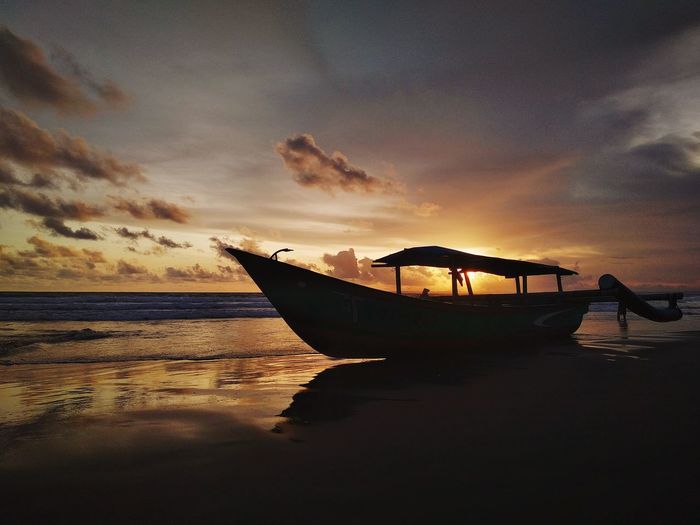 Silhouette boat moored on beach against sky during sunset