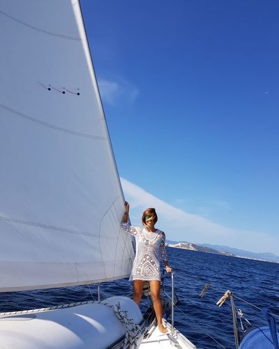 Woman standing on sailboat in sea against blue sky