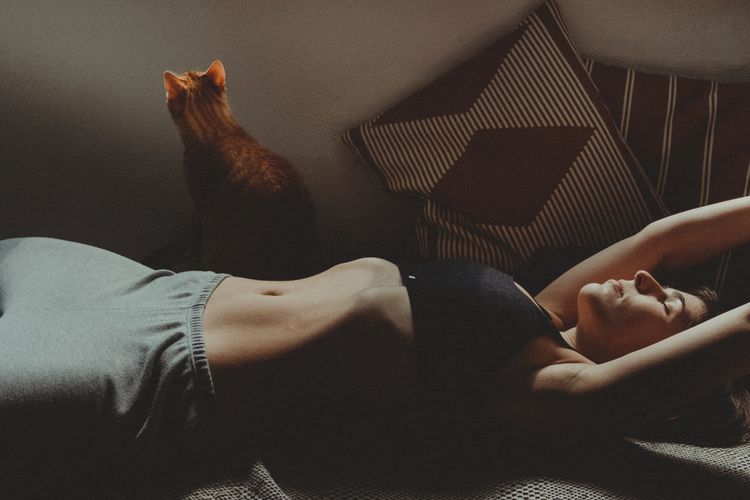 Woman lying down on sofa with cat at home