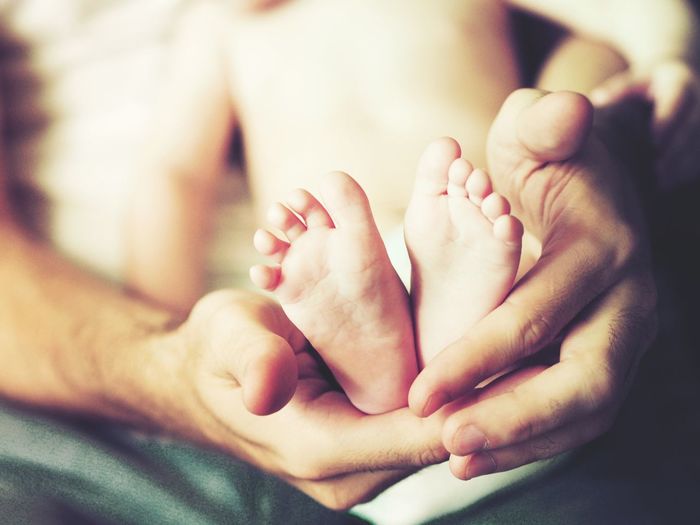 Cropped hands of parent holding baby boy leg