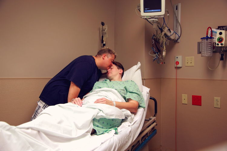 Woman kissing wife on bed in hospital