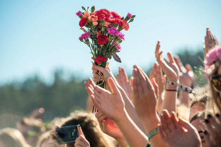 Cropped hand of person holding carnation flowers in crowd