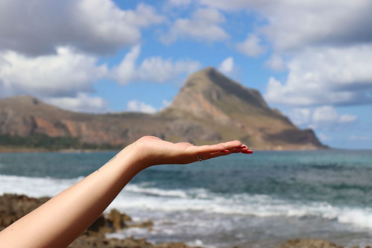 Optical illusion of woman holding mountain at sea against sky