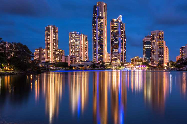 Illuminated city by river against sky at night
