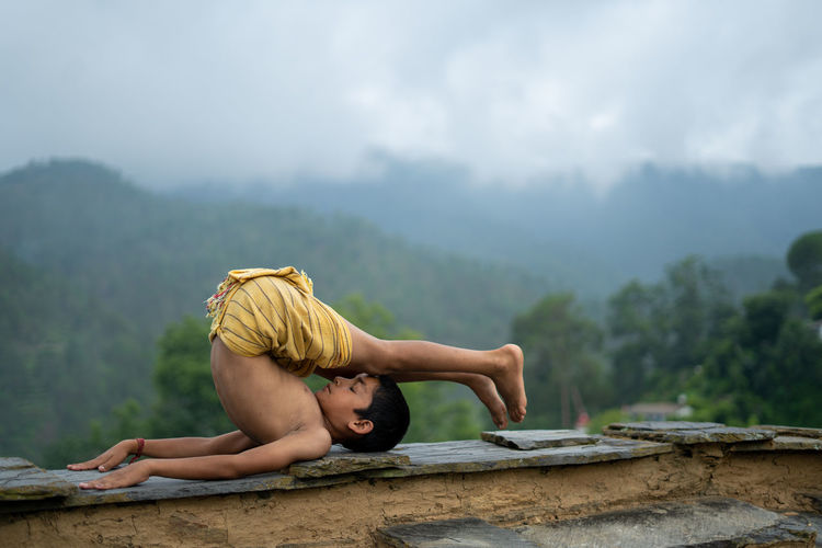 A young indian cute kid doing yoga in the mountains,wearing a dhoti