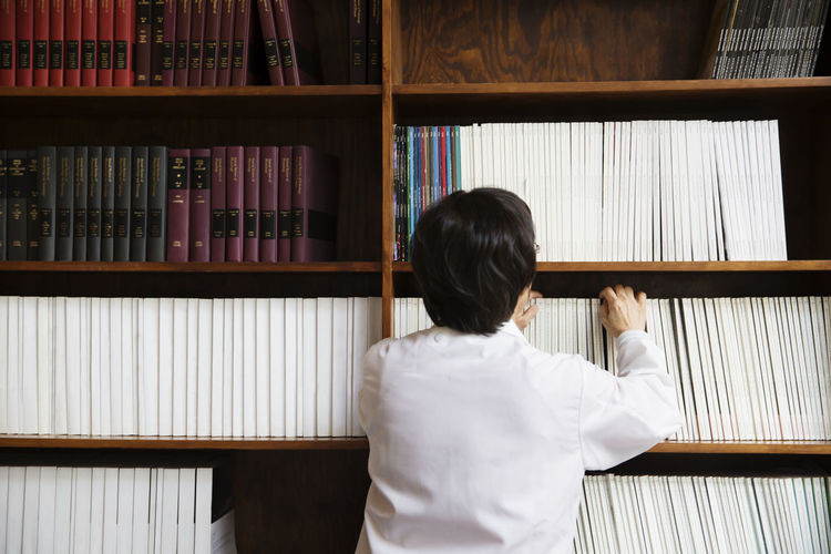 Rear view of ;senior female scientist searching book in shelf at laboratory