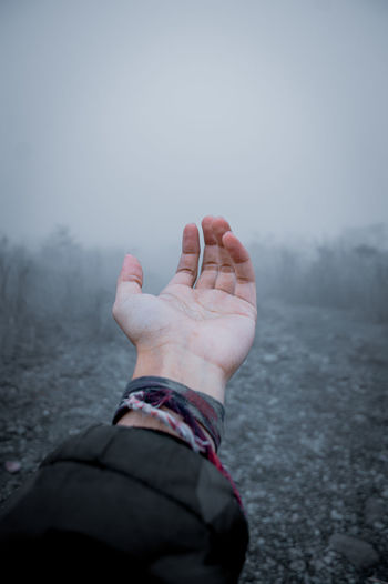 Cropped hand of person against sky during foggy weather