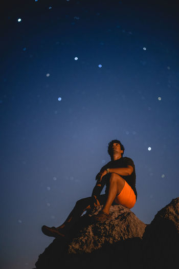 Low angle view of young sitting on rock under stars