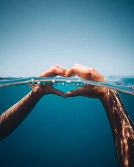 Close-up of hands making heart shape in sea against clear sky
