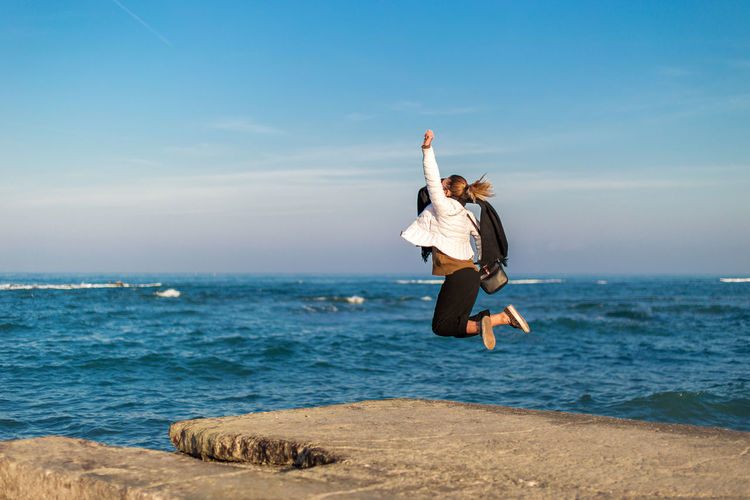 Woman jumping in mid-air at beach against sky
