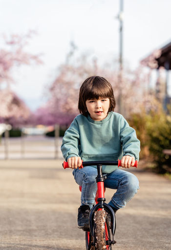 Happy cute boy riding balance bike with his legs up outdoors on spring street in city