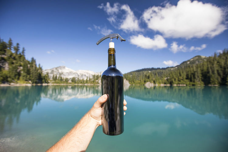 Man holding wine bottle while enjoying the lake view.