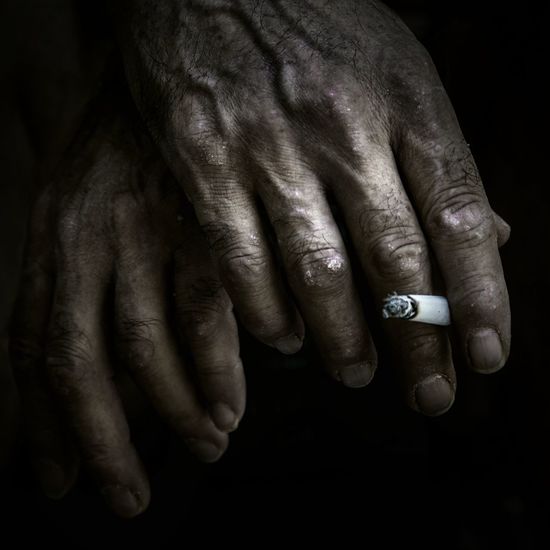 Cropped hand holding cigarette against black background
