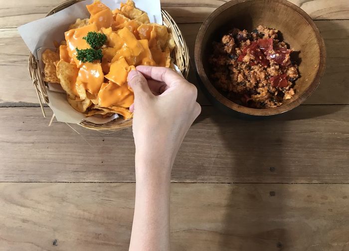 Woman holding nacho chip with its dip on wood table