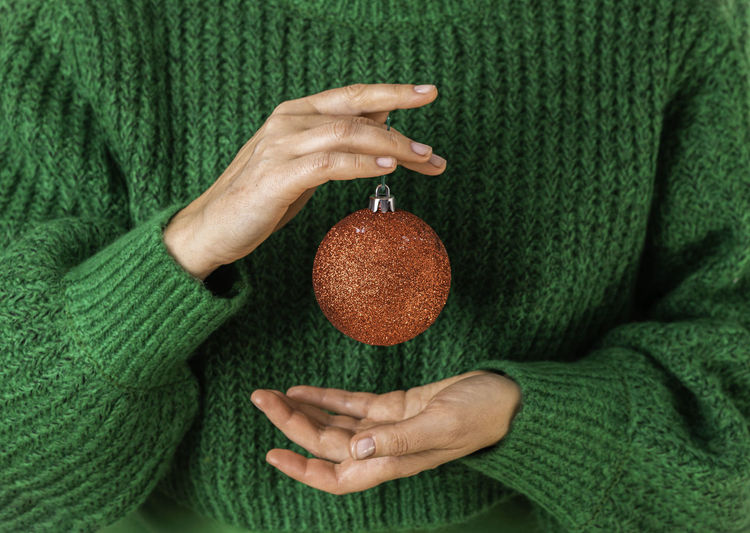 Female in green sweater are holding the symbol of the new year in their hands - a red christmas ball